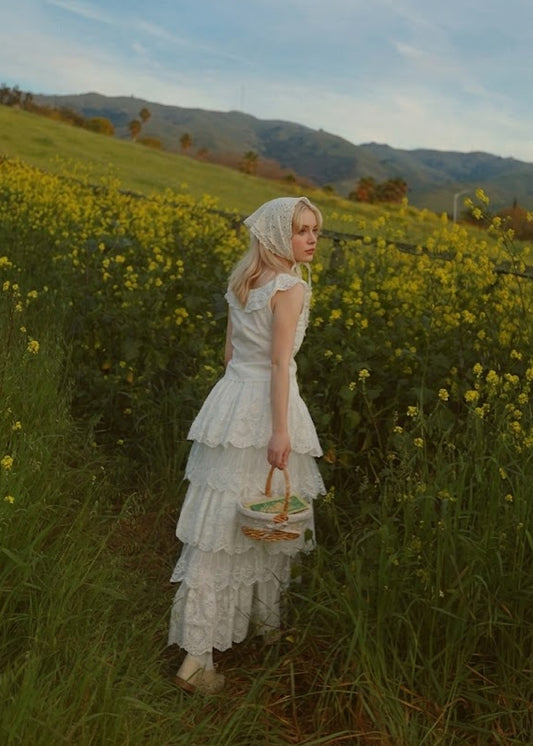 Woman in a white dress standing in a field of yellow flowers with mountains in the background