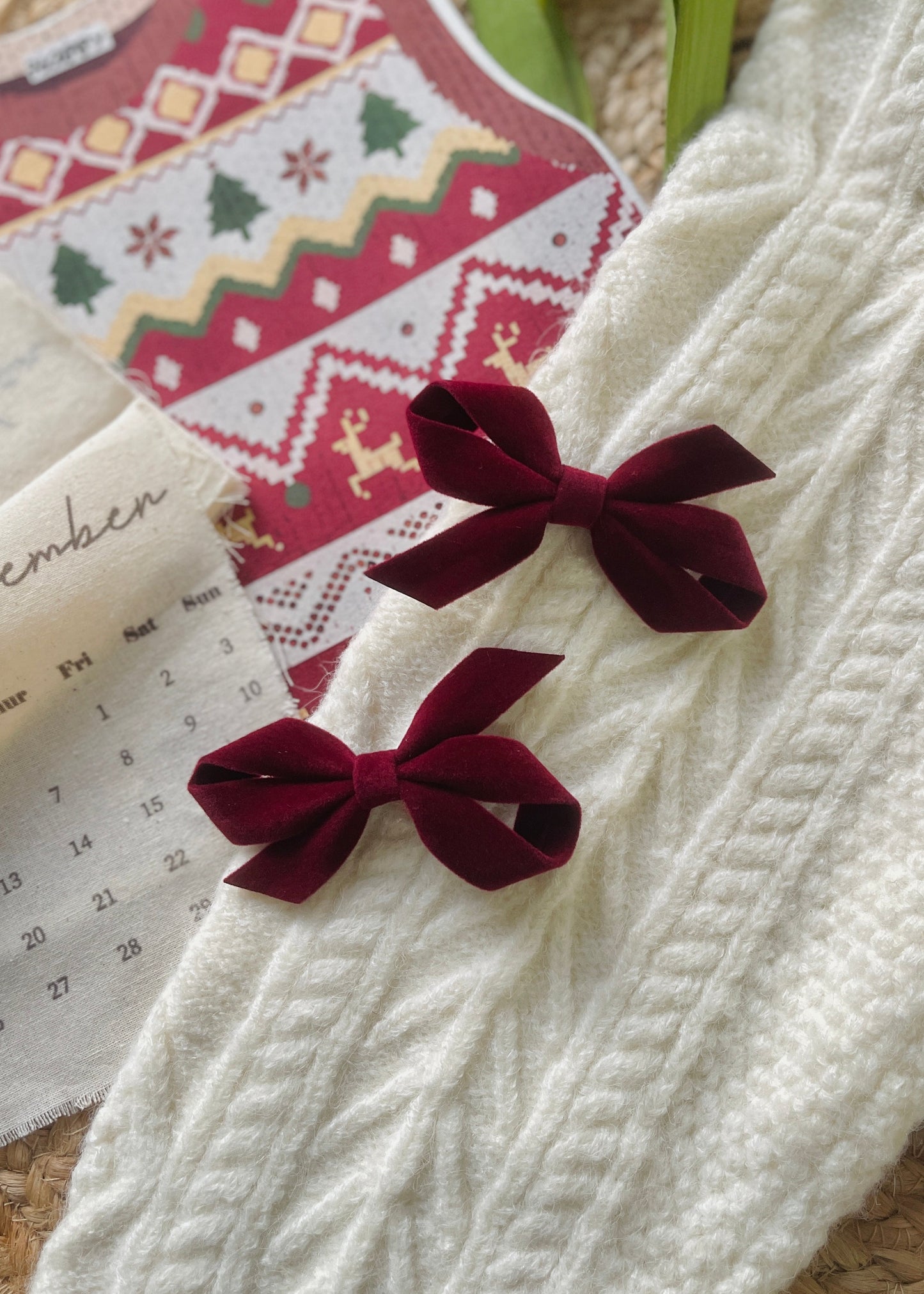 Two burgundy velvet bows on a white textured surface with a patterned card in the background.