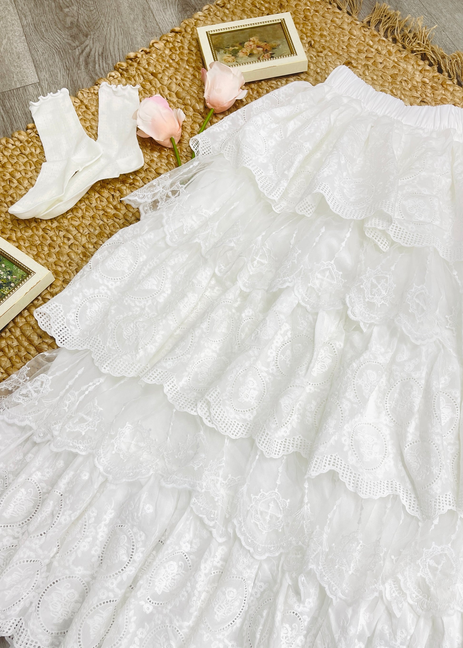 White lace dress with white socks and pink flowers on a woven mat