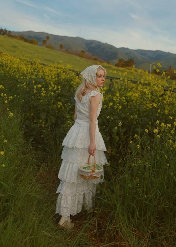 Woman in a white dress standing in a field of yellow flowers with mountains in the background