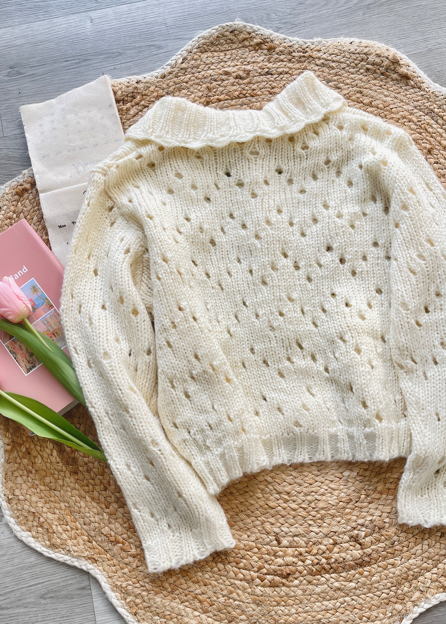 Cream-colored sweater on a textured surface with a pink box and green flowers.