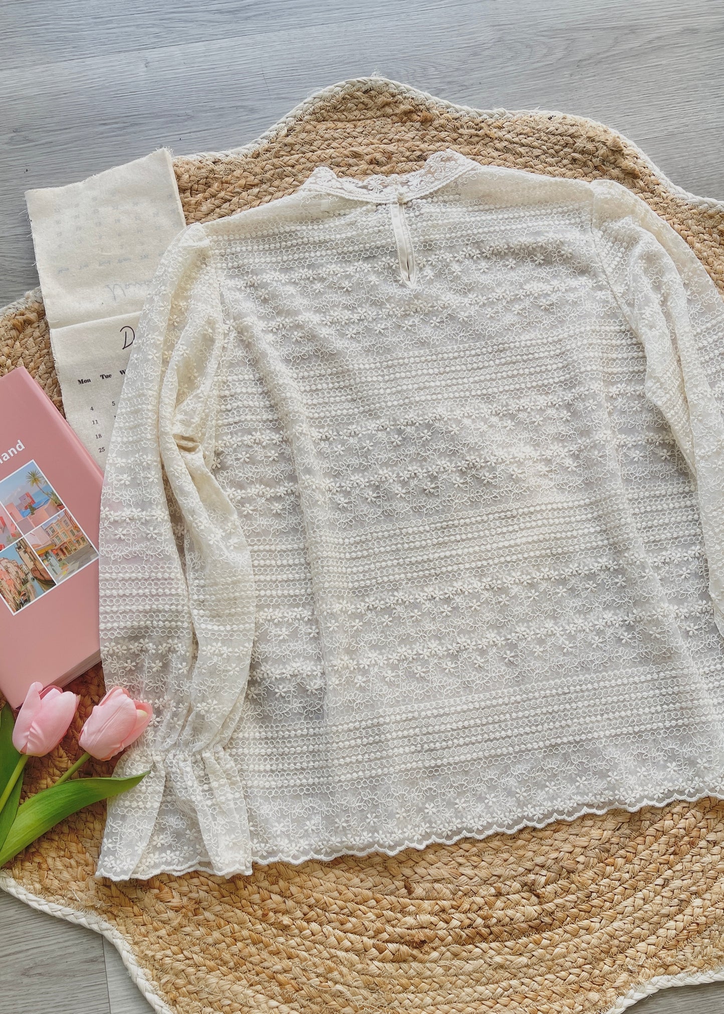 Light-colored lace top on a textured surface with pink tulips and a pink book.
